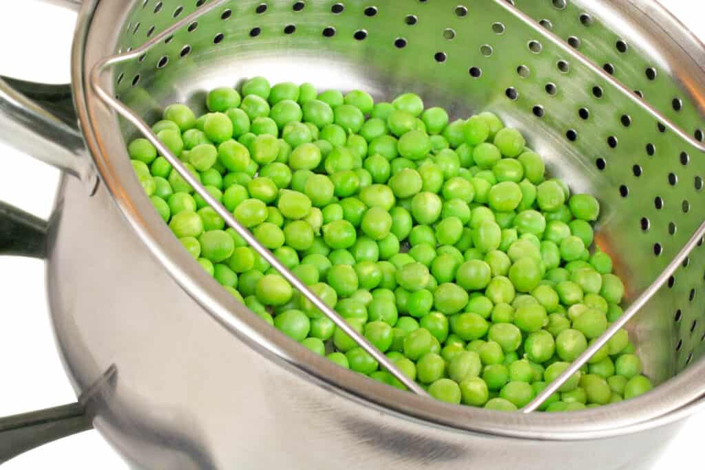 Frozen peas steaming in a pot.