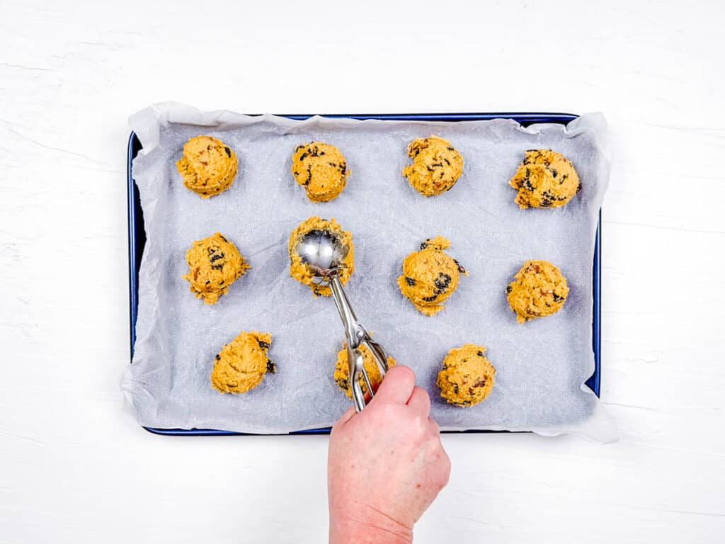 Dried fruit cookie dough being scooped onto a baking sheet.