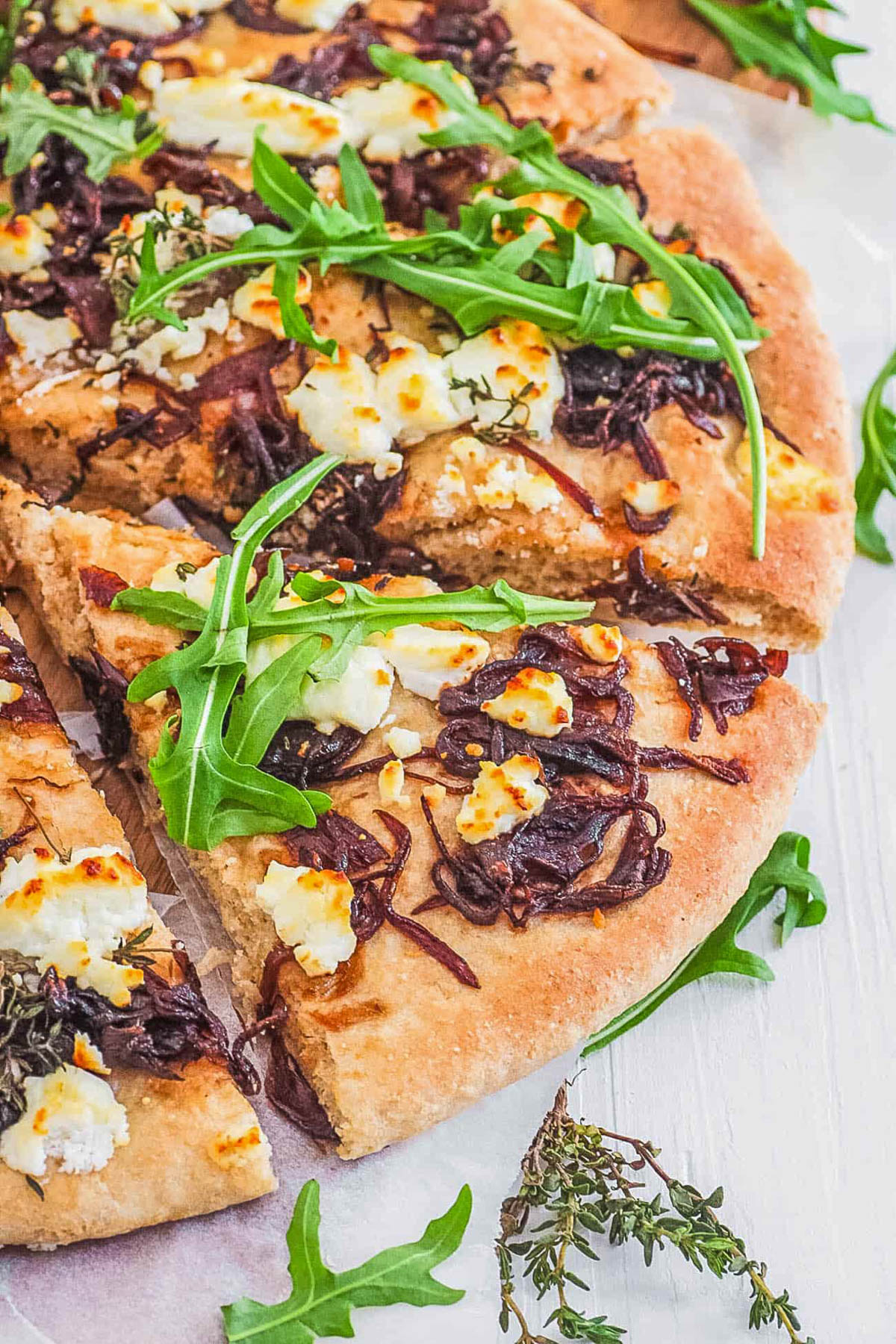 Goat cheese pizza with caramelized onions and arugula cut into slices.