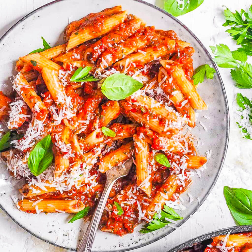 Red lentil pasta served on a white plate with homemade marinara sauce.