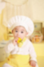 picture of baby wearing a chef hat with a yellow bell pepper to his mouth