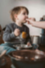 Adult hand-feeding a small boy while he mixes food in a bowl