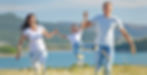 A family outside with mother and father holding son by the hands and swinging in the air