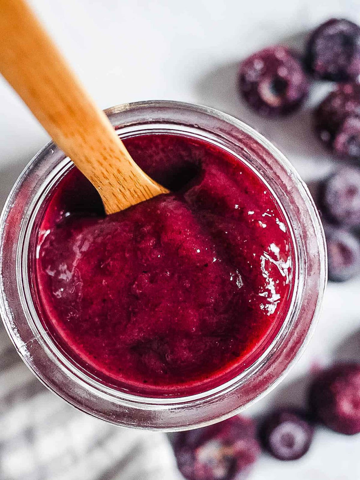 Blueberry puree for baby served in a glass jar with a wooden spoon.